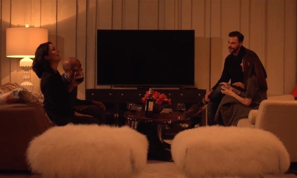 <span class="uk-h4">A group of people converse in a dimly lit room during cocktail hour.</span>