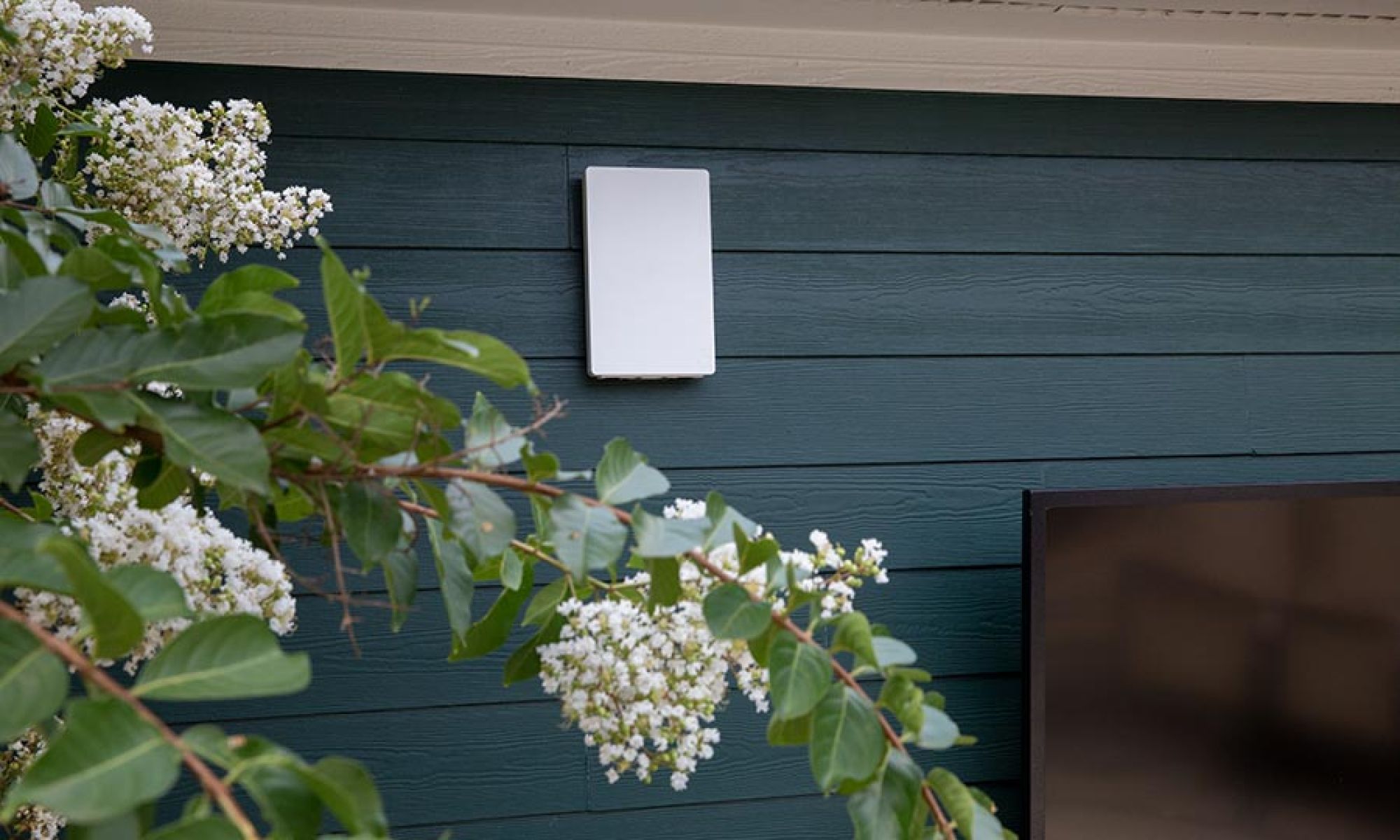 A clean, minimalistic outdoor Wi-Fi access point installed on the exterior wall of a modern home.