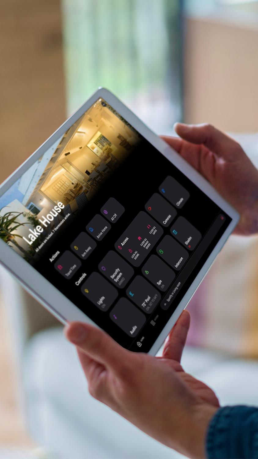 A person holding a tablet displaying a home automation interface with various control options.