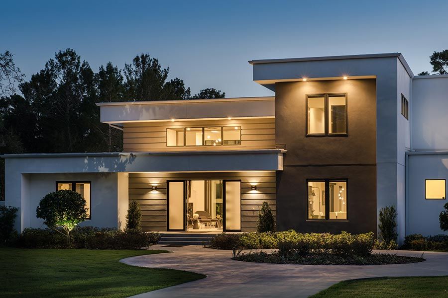 Contemporary two-story home exterior lit up warmly at dusk, surrounded by a landscaped yard.