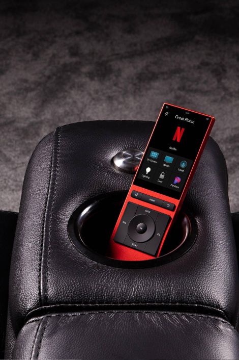 Control4 red remote on the cup holder of a black home theater seat