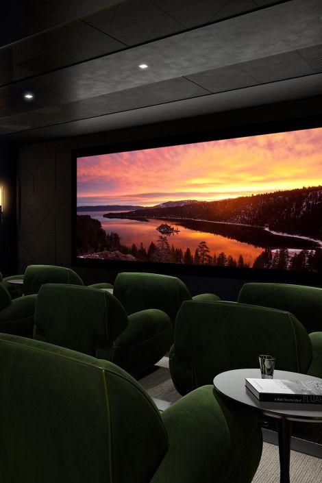 Private theater room with plush green chairs and a vibrant lake sunset displayed on screen.