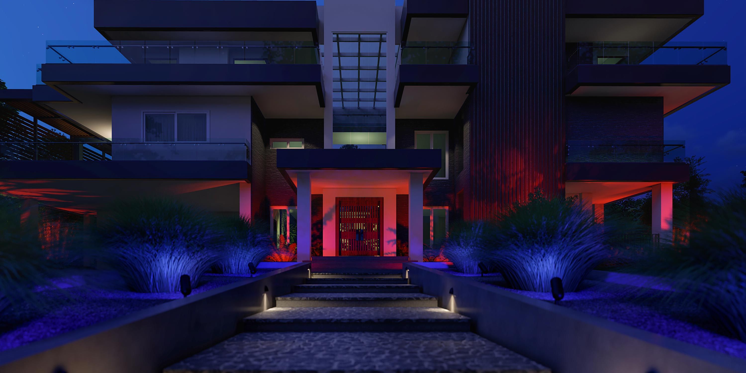 A striking modern home illuminated at night with vibrant blue and red exterior lighting accents.