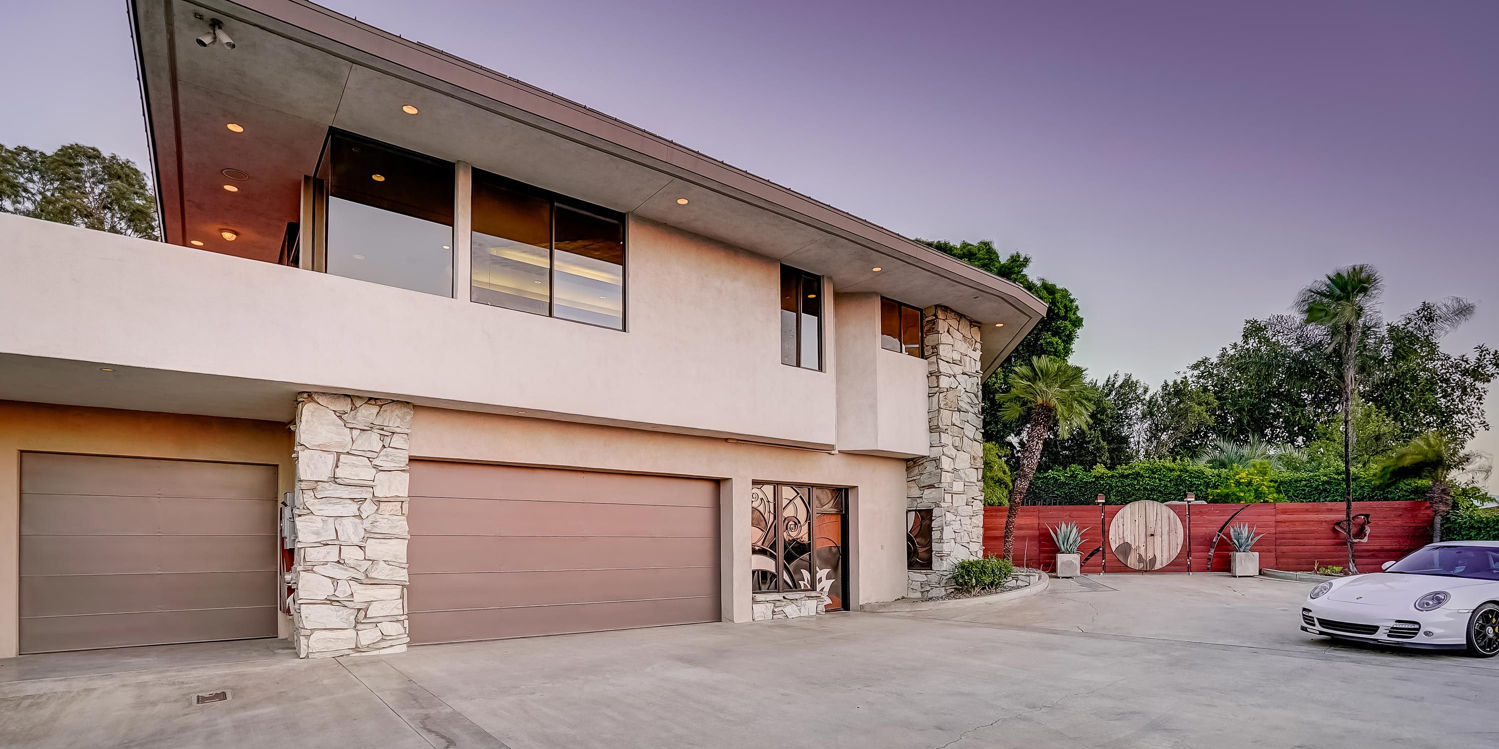 A contemporary home with a gated driveway, large garage doors, and stylish exterior lighting.