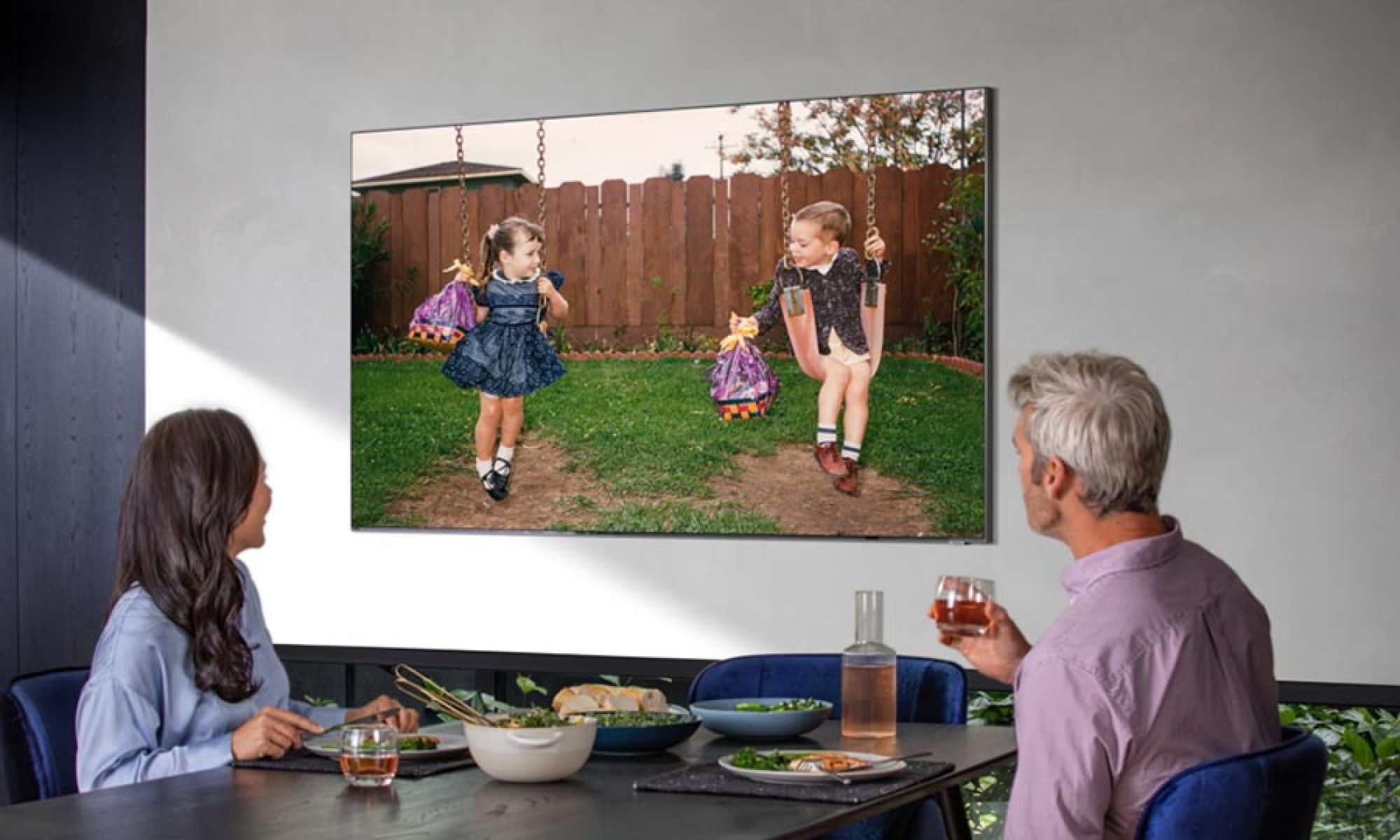 A family enjoying a meal while watching a mounted television displaying vibrant imagery.