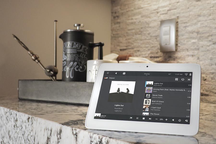 Tablet on a kitchen counter displaying a music playlist with a coffee press in the background.