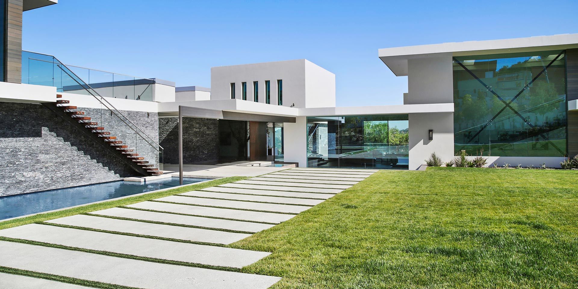 A sleek modern property with a spacious lawn, water feature, and stone-accented outdoor stairs.