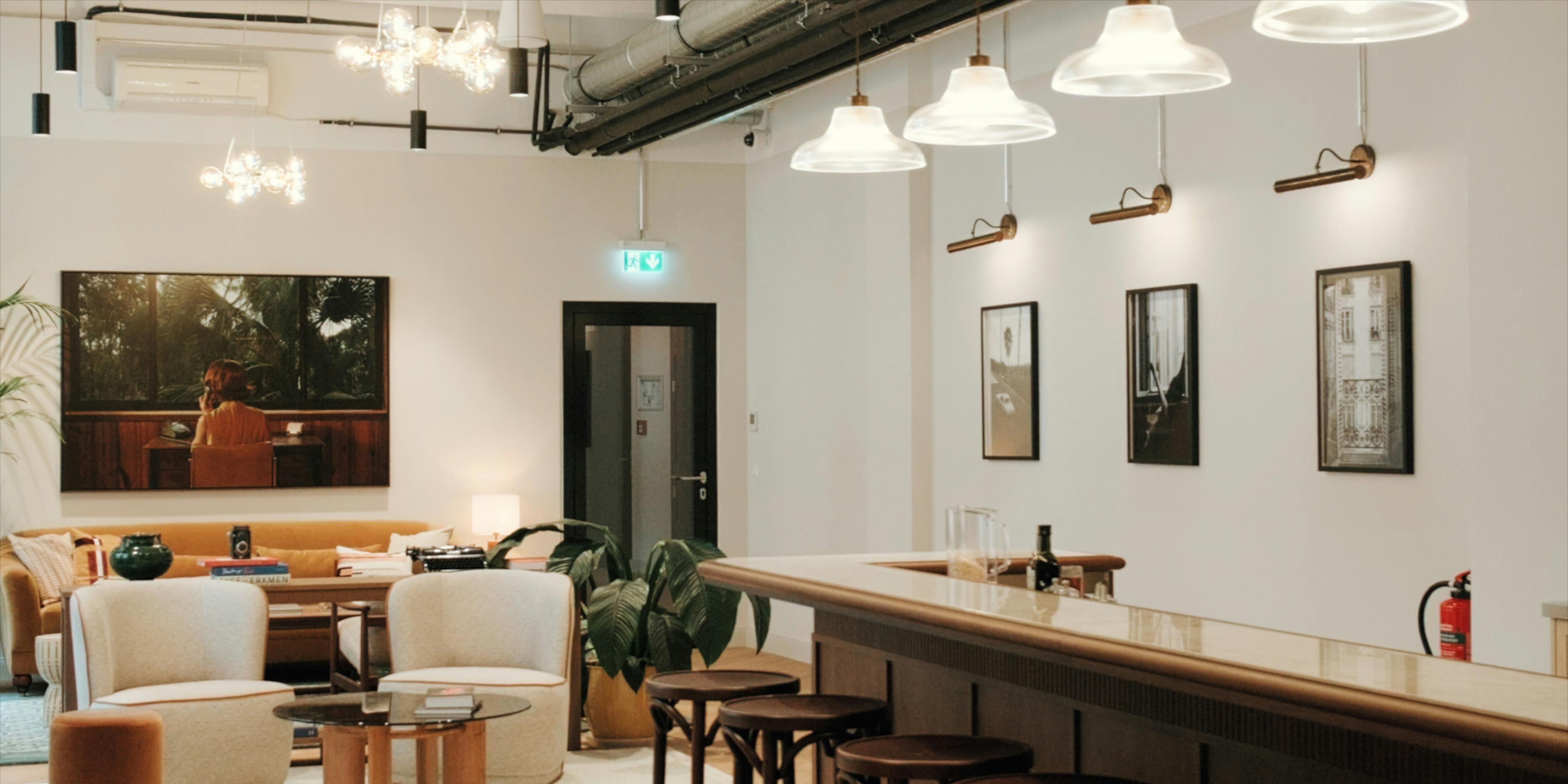 A cozy lounge area with plush chairs, a wooden bar counter, modern pendant lighting, and wall art.