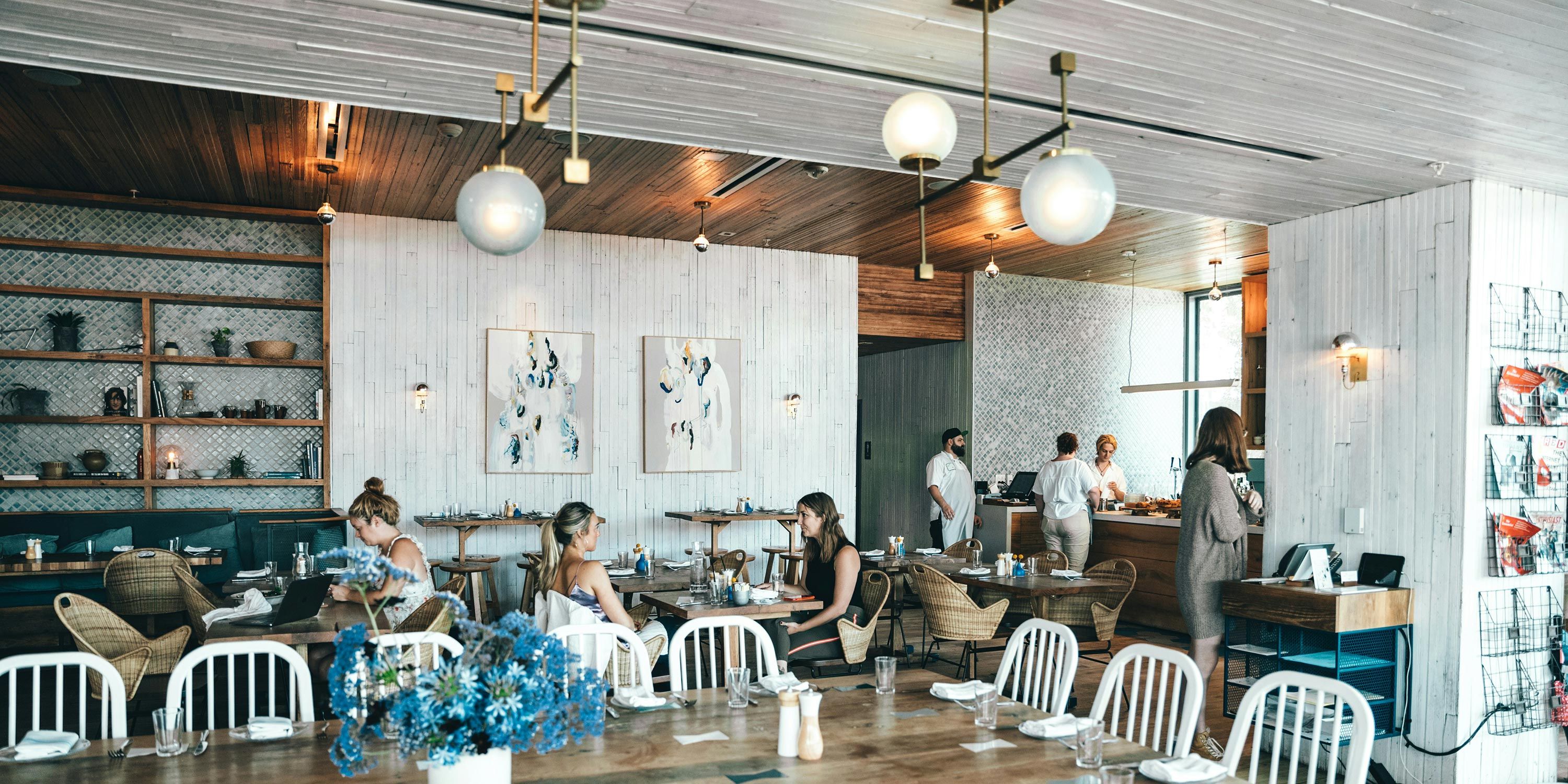 A stylish restaurant interior featuring wooden furniture, wall art, and diners enjoying their meals.