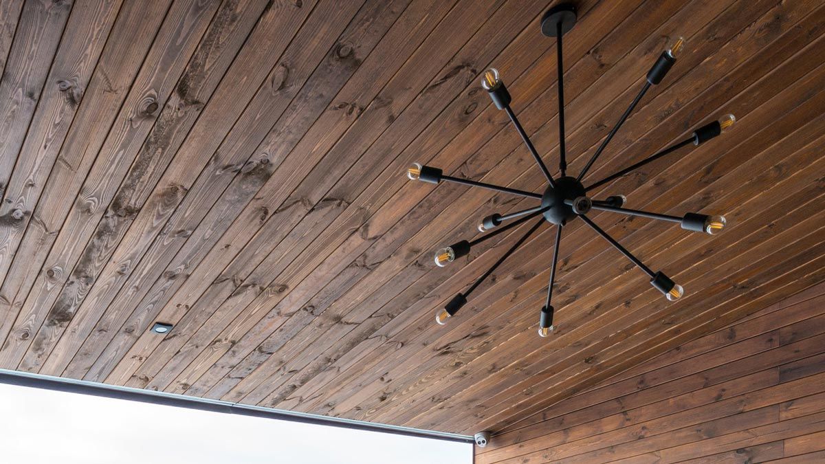 Close-up of a modern black chandelier with exposed bulbs against a wood-paneled ceiling.