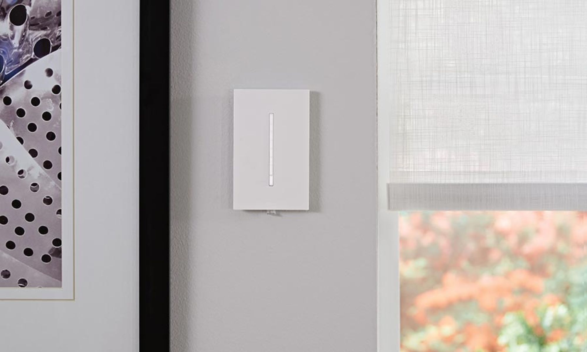 A minimalist wall-mounted lighting control switch beside a window with natural light filtering through.