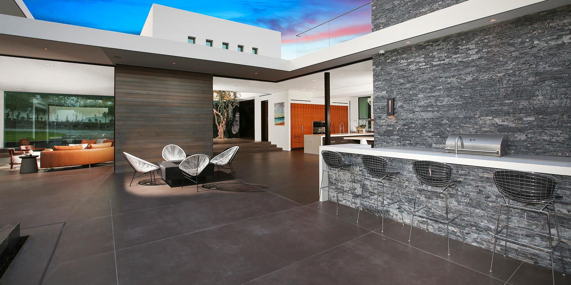 An elegant outdoor kitchen and lounge area with bar seating, modern decor, and open views.