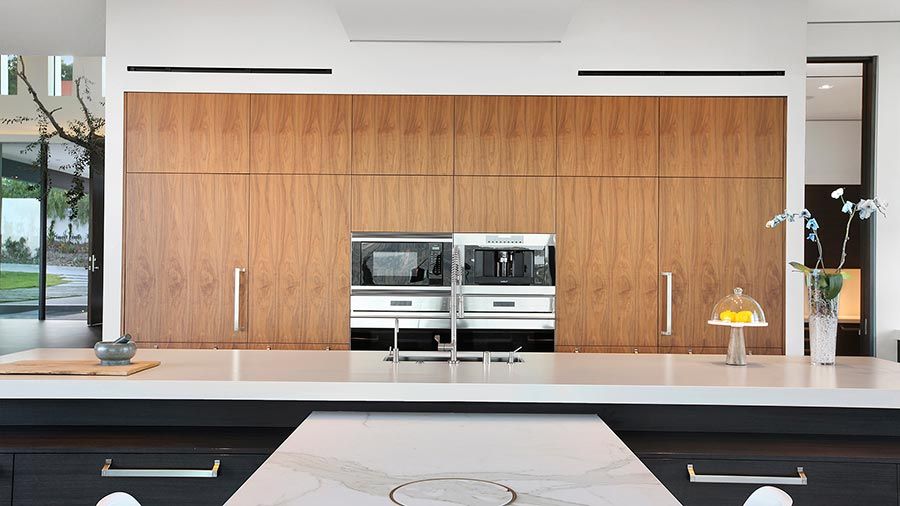 A modern kitchen with wooden cabinetry, built-in appliances, and a sleek marble island.